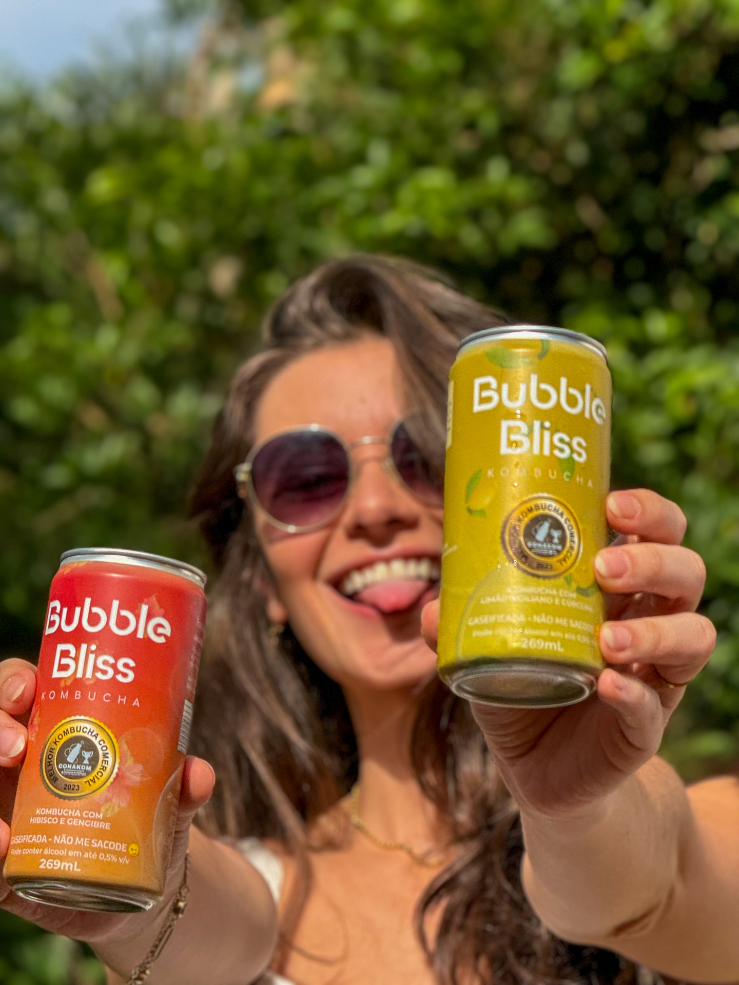 Amiga sorrindo segurando duas latas Bubble Bliss — laranja e amarela